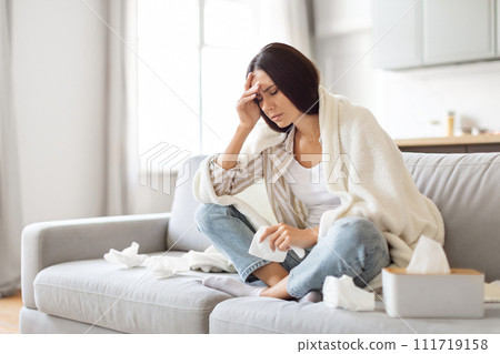 Seasonal Flu Concept. Sick Young Woman Covered In Blanket Sitting On Couch Seasonal Flu Concept. Sick Young Woman Covered In Blanket Sitting On Couch 111719158