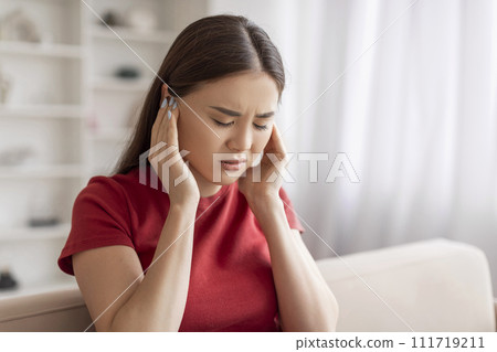 Distressed young asian woman holding her ears and grimacing in pain Distressed young asian woman holding her ears and grimacing in pain 111719211