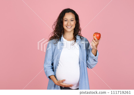 Young pregnant woman eating apple on pink background 111719261