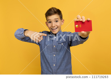 Smiling teen boy confidently pointing at red credit card in his hand 111719263