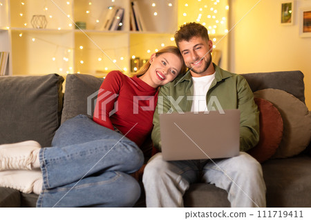 Couple with laptop enjoying time on couch, festive lights backdrop 111719411