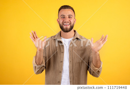 Smiling cheerful inspired handsome young european guy with beard in casual spreads arms to sides 111719448