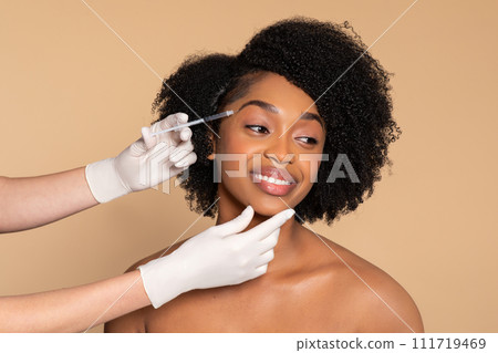 Smiling black woman during cosmetic treatment, beige backdrop 111719469