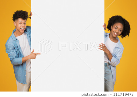 Excited African American male and female teenagers holding and pointing to a blank white banner 111719472