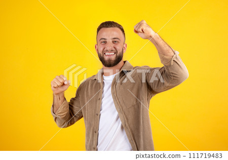 Happy millennial european man with beard in casual has fun, rise fists, celebrate win Happy millennial european man with beard in casual has fun, rise fists, celebrate win 111719483