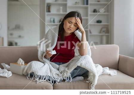 Ill asian woman with headache sitting on couch at home, Ill asian woman with headache sitting on couch at home, 111719525