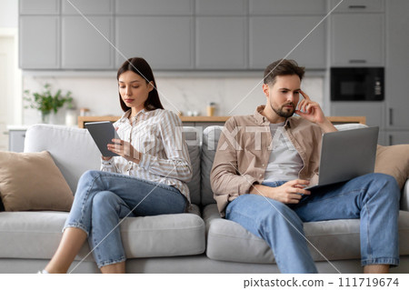 Focused european couple using tablet and laptop separately on couch 111719674