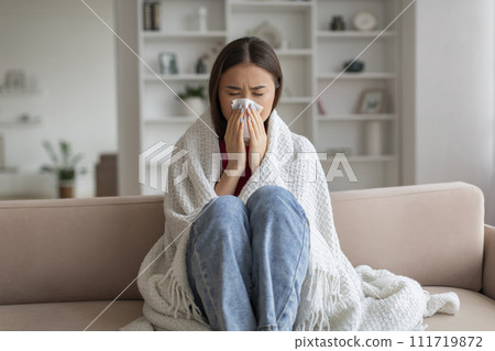 Young asian woman feeling unwell at home, sneezing into tissue 111719872