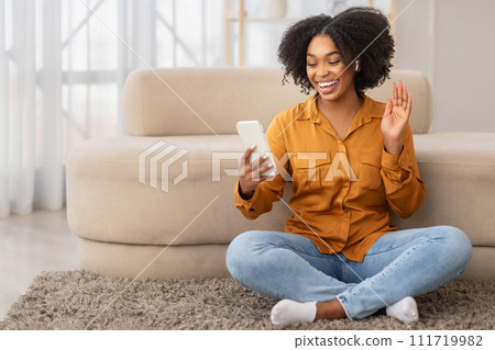 Joyful African American woman wearing a mustard shirt and blue jeans sitting cross-legged Joyful African American woman wearing a mustard shirt and blue jeans sitting cross-legged 111719982