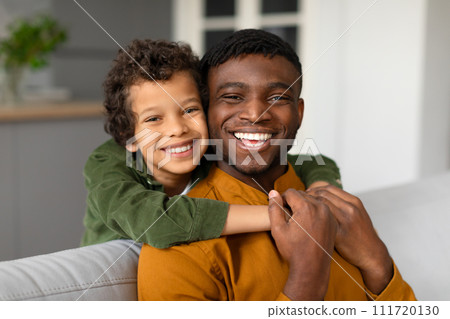 Cheerful black son hugs father from behind with bright smiles Cheerful black son hugs father from behind with bright smiles 111720130