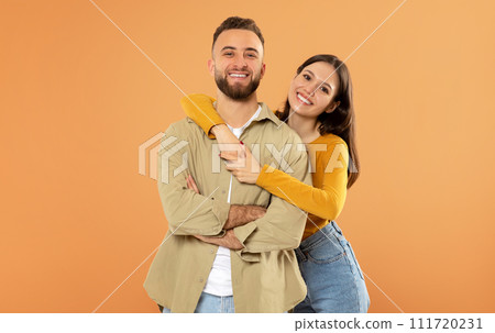 Smiling European Young Couple Hugging Over Orange Studio Background 111720231