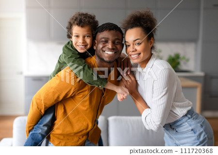 Joyful black family with young boy piggybacking on father's back 111720368