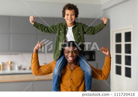 Joyful black father and son flexing muscles together at home 111720418