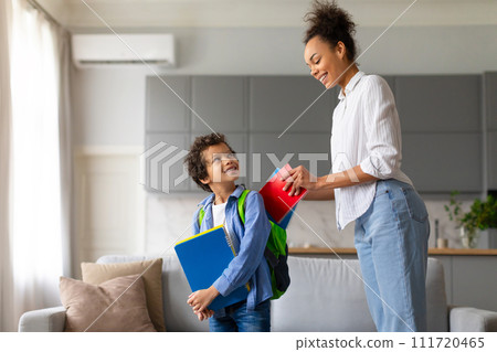 Black mother prepares son with backpack and notebooks for school Black mother prepares son with backpack and notebooks for school 111720465