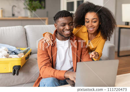 Glad african american spouses using laptop preparing for trip indoor Glad african american spouses using laptop preparing for trip indoor 111720473