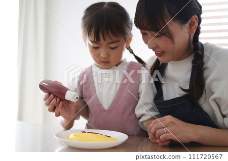 Parent and child putting ketchup on an omelet Parent and child putting ketchup on an omelet 111720567