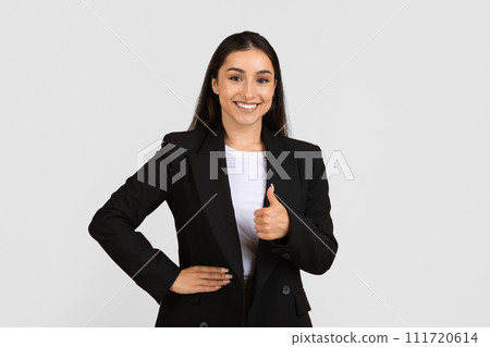 Smiling young businesswoman giving thumbs up, wearing black suit 111720614