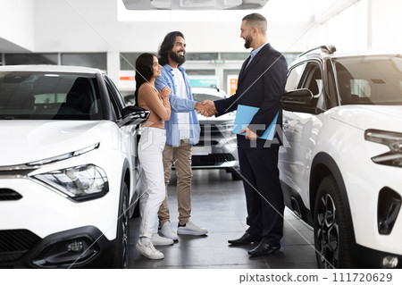 Car advisor stands discussing financing options with interested indian couple 111720629