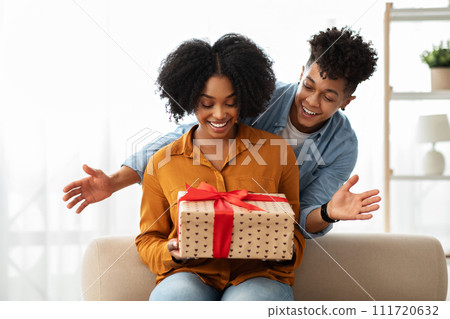 A woman seated on a sofa expresses delighted surprise, hands outstretched 111720632