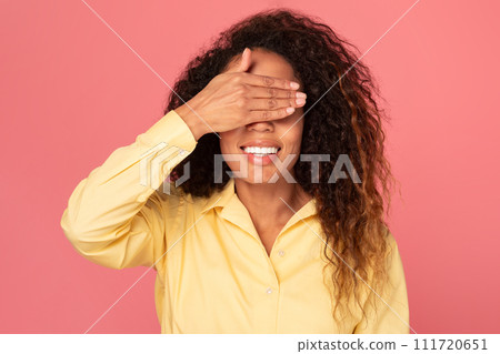 Playful black woman covering eyes with hand on pink backdrop Playful black woman covering eyes with hand on pink backdrop 111720651