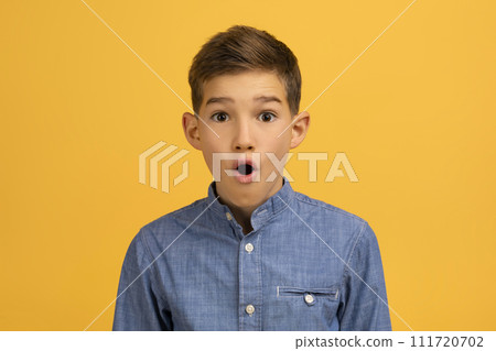 Astonished teenage boy with wide-eyed expression posing against yellow studio background 111720702