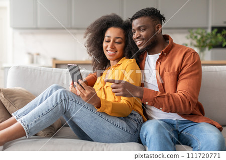 Cheerful black young couple having fun with cellphone at home 111720771