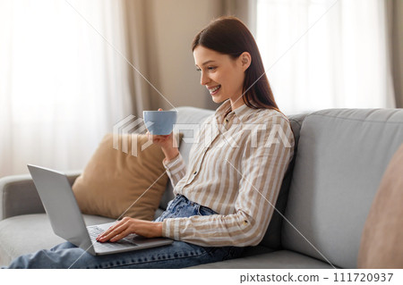 Relaxed young woman with coffee and laptop on couch 111720937