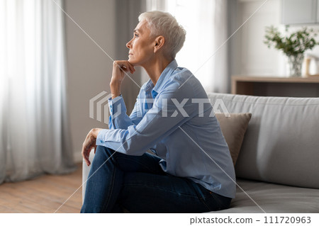 Depressed senior woman touching chin sitting on couch at home 111720963