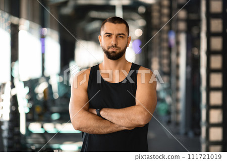 Confident muscular man in sleeveless top standing with crossed arms at gym Confident muscular man in sleeveless top standing with crossed arms at gym 111721019