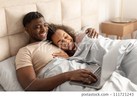 Happy black man and woman using laptop lying in bed 111721243