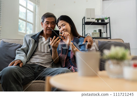 Retired elderly couple sits on couch drink tea and using mobile together and relax in their home. Senior Activity Concept 111721245