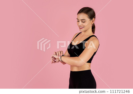 Smiling athletic woman in sportswear checking her smartwatch 111721246
