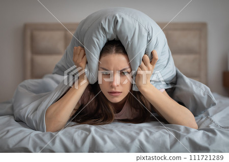 Irritated woman covering ears with pillow in bed 111721289