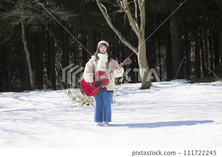 Young woman standing on the snow with a guitar Young woman standing on the snow with a guitar 111722245