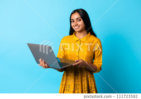 Happy middle eastern lady using laptop computer against blue backdrop 111723582