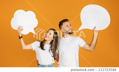 A man and woman holding blank speech bubbles overhead, looking at each other with smiles A man and woman holding blank speech bubbles overhead, looking at each other with smiles 111723589