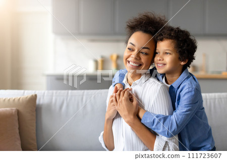 Smiling black mother and son enjoying happy embrace at home, looking at free space Smiling black mother and son enjoying happy embrace at home, looking at free space 111723607