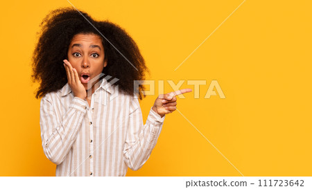Shocked black woman pointing to side on yellow background 111723642