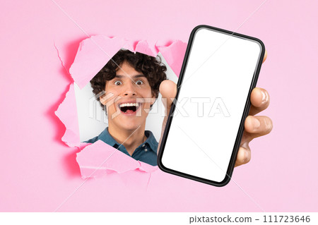 Excited guy presenting cellphone screen through hole in pink background Excited guy presenting cellphone screen through hole in pink background 111723646
