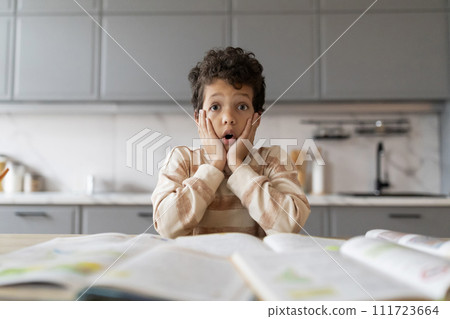 Shocked little black boy looking at workbooks and touching face Shocked little black boy looking at workbooks and touching face 111723664