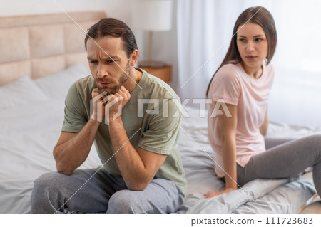 Man pondering in bed, woman sitting behind 111723683
