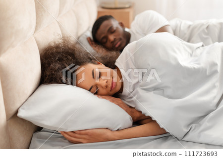 African lady hugging pillow sleeping next to her husband indoor 111723693