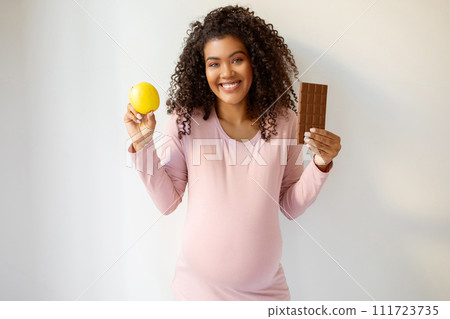 Smiling pregnant lady in pink top holding healthy apple and chocolate bar 111723735