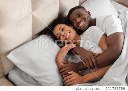 Happy millennial black couple flirting and embracing on comfortable bed Happy millennial black couple flirting and embracing on comfortable bed 111723769