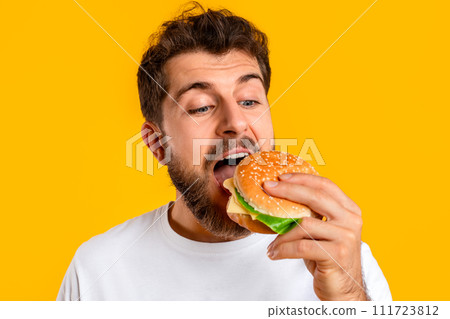 Man enjoying cheeseburger on cheat day on vibrant yellow backdrop 111723812