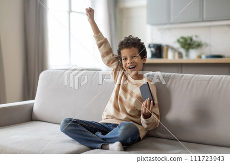 Little Black Boy Playing Games On Smartphone At Home And Celebrating Success 111723943