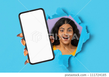 indian woman holding smartphone in hand breaking through blue background 111724185
