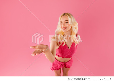 Cheerful blonde woman in pink holding open palm and showing something invisible 111724293