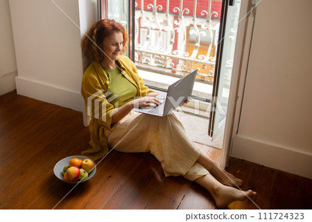 Senior woman in relaxed pose working on her laptop by balcony, Senior woman in relaxed pose working on her laptop by balcony, 111724323