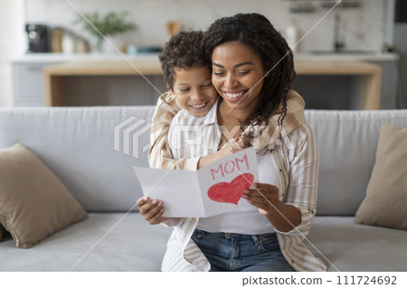Smiling black mother reading handmade heart card from her cheerful son 111724692